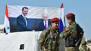 Boshpanasiz qolgan oilalar Idlib viloyatida muxolifat nazoratidagi yerlardan rejim nazoratidagi hududlarda joylashgan o‘z qishloqlariga qaytayotgan vaqtda, Suriyalik askarlar Abu al-Duhur chorrahasida Rossiya va Suriya rahbarlarining surati oldida suhbatlashib turibdi, 4-aprel. (Jorj Urfalian/AFP)