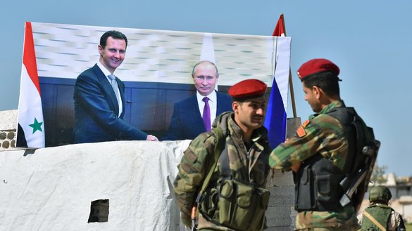 Бошпанасиз қолган оилалар Идлиб вилоятида мухолифат назоратидаги ерлардан режим назоратидаги ҳудудларда жойлашган ўз қишлоқларига қайтаётган вақтда, Суриялик аскарлар Абу ал-Дуҳур чорраҳасида Россия ва Сурия раҳбарларининг сурати олдида суҳбатлашиб турибди, 4 апрель. (Жорж Урфалиан/AFP)