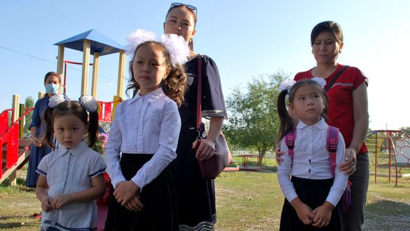 First-graders listen to a speech given by the principal during the ceremonial first-day lineup. The younger sister of one of the children came along to look at the school. September 1, K. Ibraimaliyev School, Kurpuldok village, Panfilov District, Chui Province. [Maksat Osmonaliyev]