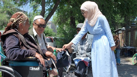 Кыргызская девушка дает милостыню двум инвалидам возле мечети 2 июня. [Максат Осмоналиев]