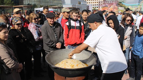 Посетители узбекского гастрономического фестиваля наблюдают за поваром, который готовит узбекский плов, прежде чем они отведают блюдо. Астана, 8 сентября. [Айдар Ашимов]
