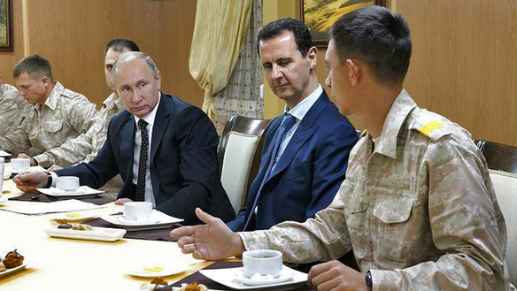 11-dekabr kuni Suriya rahbariyatining Facebook tarmog‘idagi rasmiy sahifasida e’lon qilingan tarqatma surat: Rossiya prezidenti Vladimir Putin (chapdan ikkinchi) va uning suriyalik hamkasbi Bashar Asad (o‘ngdan ikkinchi) Suriyaning Latakiya viloyatida joylashgan Xmeymimdagi Rossiya aviabazasida rossiyalik harbiy zobitlar uchrashmoqda. (Suriya rahbariyatining Facebook sahifasi/AFP)