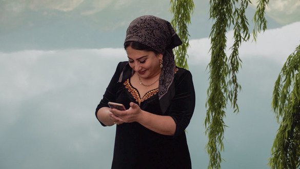 Женщина в традиционной одежде проверяет прогноз погоды на мобильном телефоне в Нуреке, Таджикистан. [Кристина Штульбергер / Zoï Environment Network].