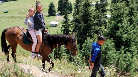 Девочки на лошади спускаются с горы. В последние годы, по мере роста туризма в джайлоо Кок-Жайык, местные жители научились зарабатывать деньги, предлагая различные услуги. Одна из них — предоставление туристам лошадей для верховой езды. Кылыч, владелец одной из лошадей, берет 300 сомов (3,90 доллара США) за то, чтобы по горным тропам провести всадников от джайлоо к водопаду. Ущелье Джеты-Огуз, Иссык-Кульская область, 25 июля. [Максат Осмоналиев]