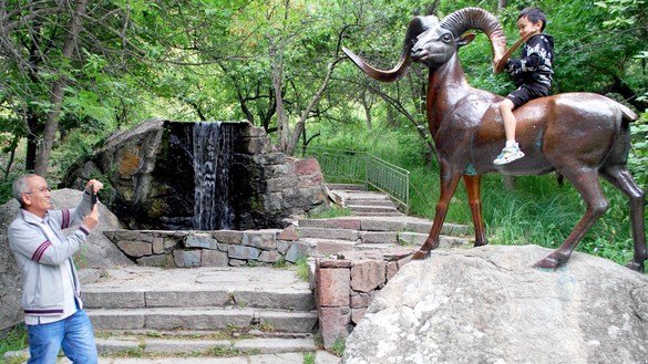 A grandfather photographs his grandson on a bronze sculpture of a mountain sheep. "Because of the restrictions related to the pandemic, instead of filling to our capacity of 300 people, the Issyk-Ata resort has welcomed only 100 guests," said G. Asakeyeva, the head doctor at the resort. Issyk-Ata resort, Chui Province, July 27. [Maksat Osmonaliyev]