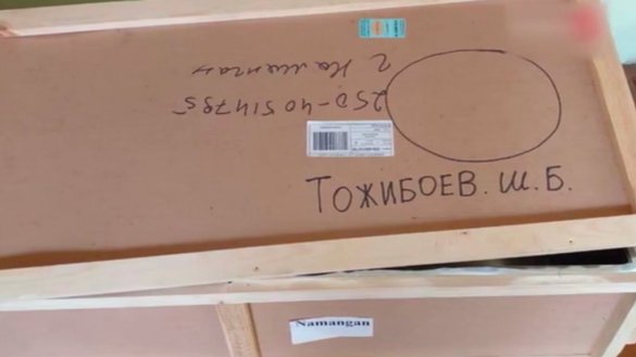 Деревянный ящик с указанием места доставки (Наманган), именем Тожибоева, комбинацией из 12 цифр, неопределенной круглой отметкой и двумя наклейками, прочитать которые невозможно из-за плохого качества снимка.
